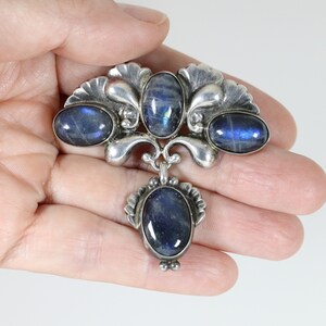 Puede incluir: Un broche de plata con cuatro piedras azules ovaladas. El broche tiene un dise&ntilde;o decorativo con un motivo floral.
