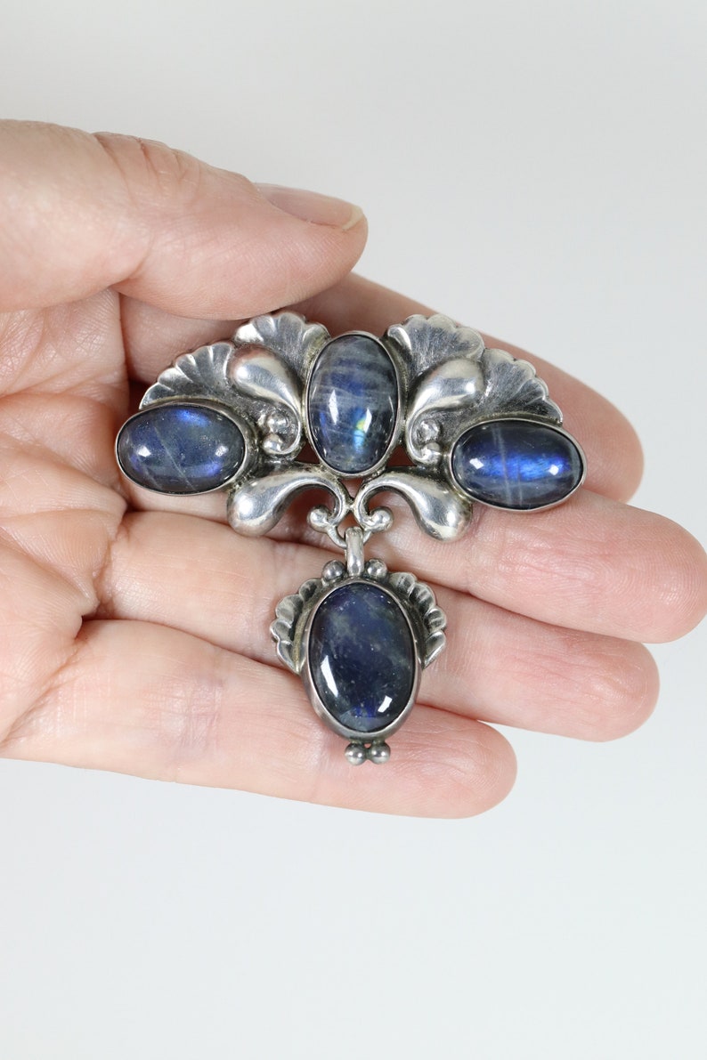 Puede incluir: Un broche de plata con cuatro piedras azules ovaladas. El broche tiene un dise&ntilde;o decorativo con un motivo floral.