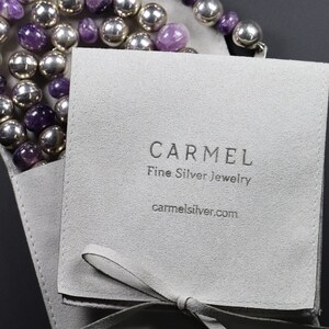 Puede incluir: Una bolsa de joyer&iacute;a de gamuza gris con cierre de cinta blanca. La bolsa tiene el texto "CARMEL Fine Silver Jewelry carmelsilver.com" impreso en la parte delantera.