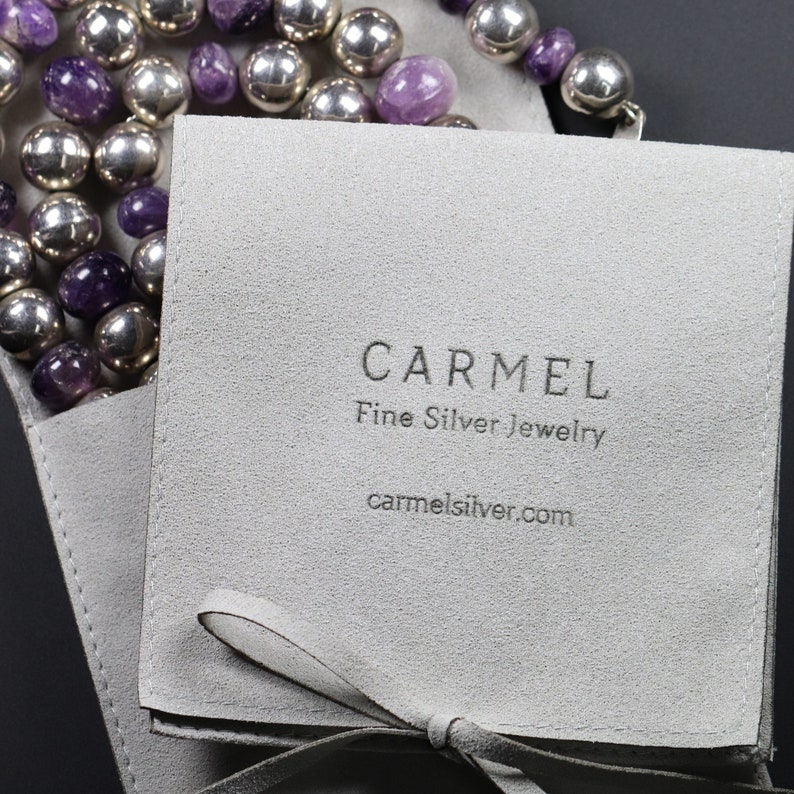 Puede incluir: Una bolsa de joyer&iacute;a de gamuza gris con cierre de cinta blanca. La bolsa tiene el texto "CARMEL Fine Silver Jewelry carmelsilver.com" impreso en la parte delantera.