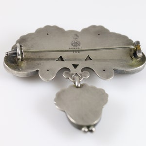 Puede incluir: Broche de plata con un dise&ntilde;o floral y un colgante. La broche tiene un pasador y un cierre de plata. La parte posterior de la broche est&aacute; marcada con "925" y "ARIZONA".
