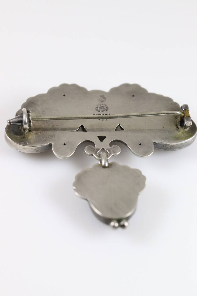 Puede incluir: Broche de plata con un dise&ntilde;o floral y un colgante. La broche tiene un pasador y un cierre de plata. La parte posterior de la broche est&aacute; marcada con "925" y "ARIZONA".