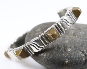 May include: A silver bracelet with brown square-shaped stones set into the metal. The bracelet has a wavy design on the metal.