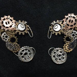Könnte beinhalten: Ein Paar silberne und kupferne Steampunk-Ohrmanschetten mit Zahnrädern, Blättern und einem weißen Perlenakzent.