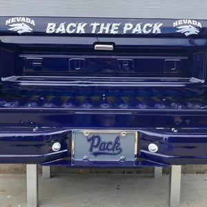 May include: A blue Ford pickup truck bed with a white "BACK THE PACK" and "NEVADA" decals. The truck has a license plate frame that says "Pack" in blue letters.