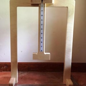 May include: A wooden measuring tool with a vertical ruler and a sliding mechanism. The tool is made of light-colored wood and has a rectangular frame. The ruler is marked with inch increments.