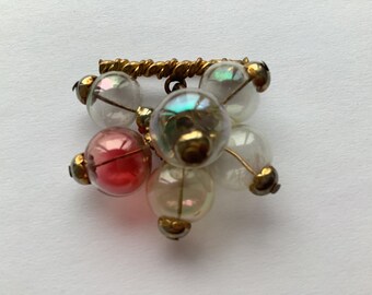 May include: A cluster of iridescent glass beads with a pink bead in the center, connected by gold wire and a gold bar.