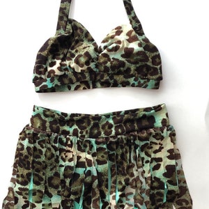 May include: A green and brown leopard print bikini top and skirt with a fringed bottom. The skirt has a high waist and the top has a halter neck.