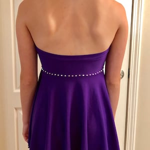May include: A purple halter dress with a fitted bodice and a flared skirt. The dress is decorated with a row of rhinestones around the waist and a row of rhinestones around the hem.