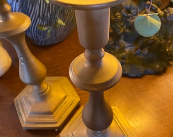 May include: Two gold metal candle holders with a hexagonal base and a round top. The candle holders are on a wooden surface.