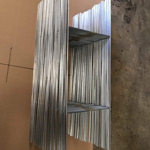 May include: A bundle of silver metal rods stacked together in a rectangular shape. The rods are arranged in a grid pattern, with some of the rods extending beyond the others.