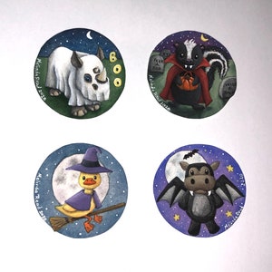 May include: Four hand-painted round ornaments featuring Halloween-themed characters. The ornaments are decorated with a white rhinoceros wearing a ghost costume, a skunk wearing a vampire costume, a duck wearing a witch's hat and a hippopotamus wearing a bat costume. Each ornament has a blue background with stars and a moon.