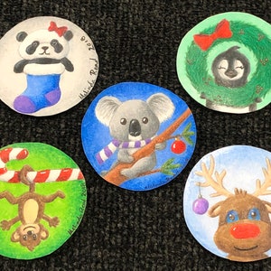 May include: Five hand-painted round ornaments with a Christmas theme. The ornaments feature a panda bear in a stocking, a koala bear holding a red ornament, a penguin in a green wreath, a monkey hanging from a candy cane, and a reindeer with red antlers and a red nose.