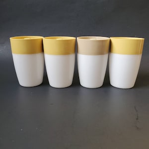 May include: Four ceramic mugs with a two-tone design. The mugs have a white bottom and a yellow or brown top.