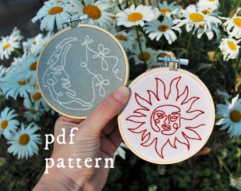 May include: Two embroidery hoops with white fabric. The hoop on the left has a gray background with a white line drawing of a crescent moon with a face and flowers. The hoop on the right has a white background with a red line drawing of a sun with a face. The text "pdf pattern" is below the hoops.