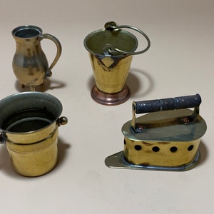 May include: Four miniature brass kitchen items: a pitcher, a bucket with a handle, a small bucket, and a flat iron with a wooden handle.