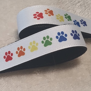 May include: White key chain with a rainbow paw print design. The key chain is made of white ribbon with black backing and a silver metal key ring.