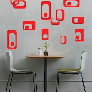 May include: A white wall with red geometric shapes, two chairs with black legs, and a table with a wooden top and black legs.