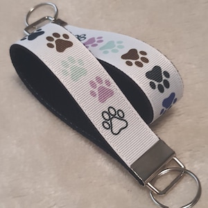 May include: White and black key chain with a black and white paw print design. The key chain has a black strap and a silver key ring.