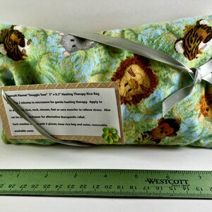 May include: A green and blue patterned heating therapy rice bag with animal illustrations, tied with a silver ribbon. The bag is approximately 5 inches by 8.5 inches. A tag with product information is attached.