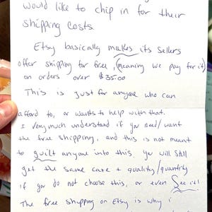 May include: Handwritten note with text about Etsy shipping costs. The note explains the option to contribute to shipping fees, the free shipping policy for orders over $35, and the reasons for not offering sales due to shipping costs.