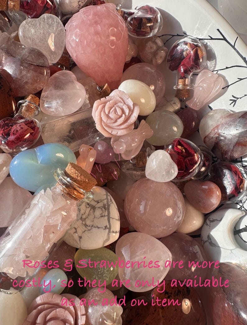 May include: A collection of various pink and clear crystals, including heart-shaped stones, spheres, and a carved rose. Small glass bottles with cork stoppers are also visible, some filled with dried rose petals. The text in the image reads "Roses & Strawberries are more costly, so they are only available as an add on item."