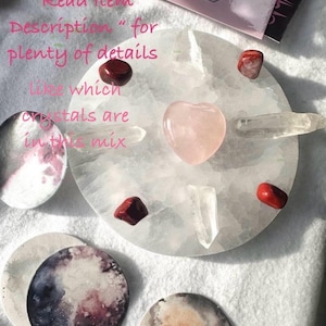 May include: A white, round selenite charging plate with a pink heart-shaped crystal, red and clear crystals, and moon-themed coasters. The image includes text that reads "Please click on 'Read Item Description' for plenty of details like which crystals are in this mix."