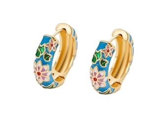 May include: A pair of gold hoop earrings featuring a bright blue enamel base with a colorful floral pattern. The design includes white and pink petals with green leaves and small red accents. These earrings have a hinged closure mechanism.
