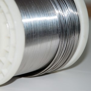 May include: A spool of silver-colored wire wound tightly around a white plastic core.