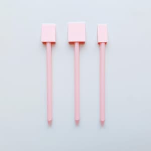 May include: Three pink plastic craft tools with square tips and long handles.