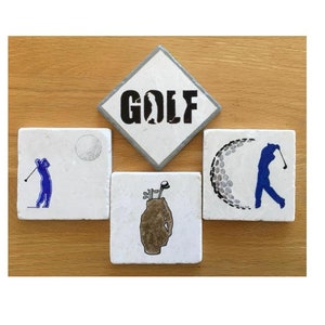 May include: Four white square coasters with golf-themed designs. One coaster has the word "GOLF" in black lettering. Another coaster has a golfer swinging a club. A third coaster has a golf ball with a dimpled surface. The final coaster has a golf bag with clubs.