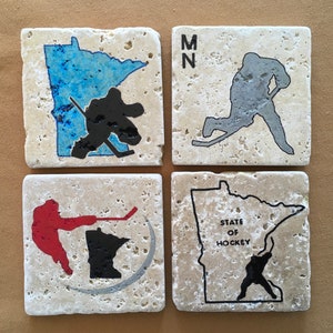 May include: Set of four coasters featuring the state of Minnesota. Each coaster has a different design, including a hockey player silhouette, the state outline, and the text "State of Hockey".