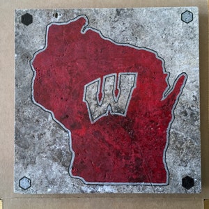 May include: A gray and red Wisconsin state outline with a white "W" inside. The outline is on a gray stone background with black hexagonal accents.