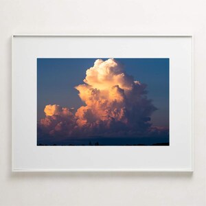 May include: A large, fluffy cumulus cloud illuminated by the setting sun, casting a warm orange glow against a blue sky.