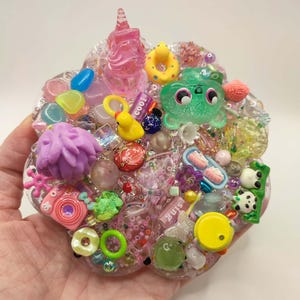May include: A clear resin art piece with various colourful miniature objects embedded within. Includes a pink unicorn, yellow duck, green frog, and other small charms. The word "cool" is visible.