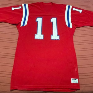 May include: A red jersey with the number 11 in white on the front and back. White and blue stripes accent the shoulders. The number 1 is on each sleeve. The jersey is made of a breathable mesh fabric.