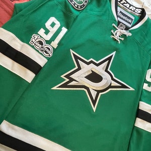 May include: Green Dallas Stars hockey jersey with white and black accents. Features the number 91 on the sleeve and a large star logo on the front. Includes the Reebok and NHL logos.