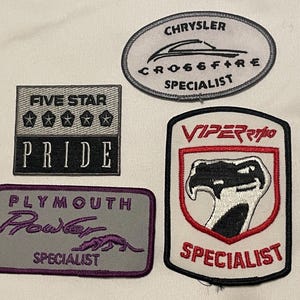 May include: Four embroidered patches with automotive themes. One patch reads "CHRYSLER CROSSFIRE SPECIALIST" in white on a grey oval. Another says "FIVE STAR PRIDE" with stars. A third patch says "PLYMOUTH POWER SPECIALIST". The last patch says "VIPER SPECIALIST".