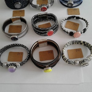 May include: Assortment of ten bracelets with different designs and colors. Each bracelet has a unique charm in the center. The bracelets are arranged in rows on a white surface.
