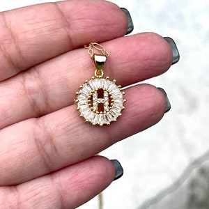 May include: Gold chain necklace with a pendant featuring the letter H surrounded by clear cubic zirconia stones.