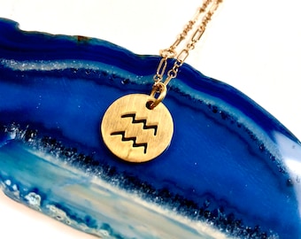 May include: Gold necklace with a round pendant featuring the Aquarius zodiac symbol on a blue agate background.