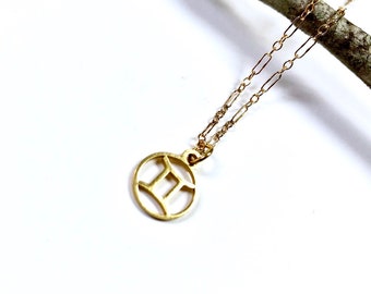 May include: A gold necklace with a circular pendant featuring the Gemini zodiac symbol. The chain is a delicate, linked style.
