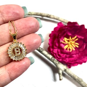 May include: Gold necklace with a pendant featuring the letter B surrounded by clear baguette-shaped crystals.