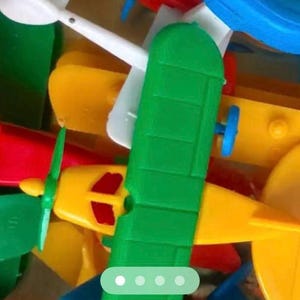 May include: A collection of colorful toy airplanes in various colors, including yellow, green, red, and blue. The planes have propellers and wings, suggesting a playful theme. The image is a close-up, highlighting the details of the plastic toy aircraft.