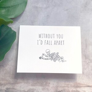 May include: A white card with black text that reads "Without you I'd fall apart". A simple black line drawing of a skeleton falling apart is below the text.