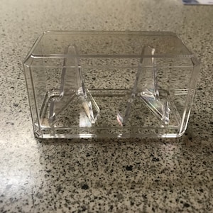 May include: A clear plastic display case with two clear plastic stands inside. The case is rectangular and has a clear lid.