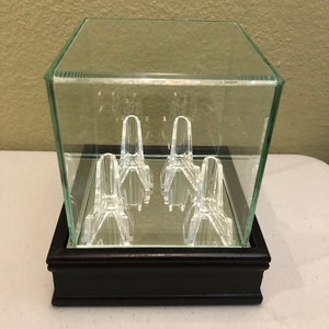 May include: A clear glass display case with a black wooden base. The case has a mirrored bottom and features six clear acrylic display stands inside.