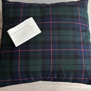 May include: A square pillow cover featuring a dark green, navy blue, and black plaid pattern with thin red accent lines. A white paper note is attached to the front with the handwritten text: fabric case only - Pillow stuffing not included.