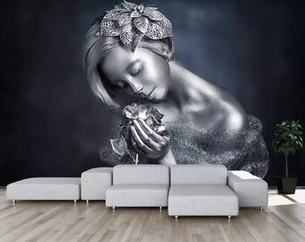 May include: A silver-painted woman with a silver flower crown holds a silver rose in her hands. The background is a dark gray with a hint of blue.