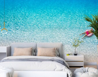 May include: A bedroom with a white bed and a blue and white beach scene mural on the wall. The mural features a person floating on an inflatable ring in the ocean.